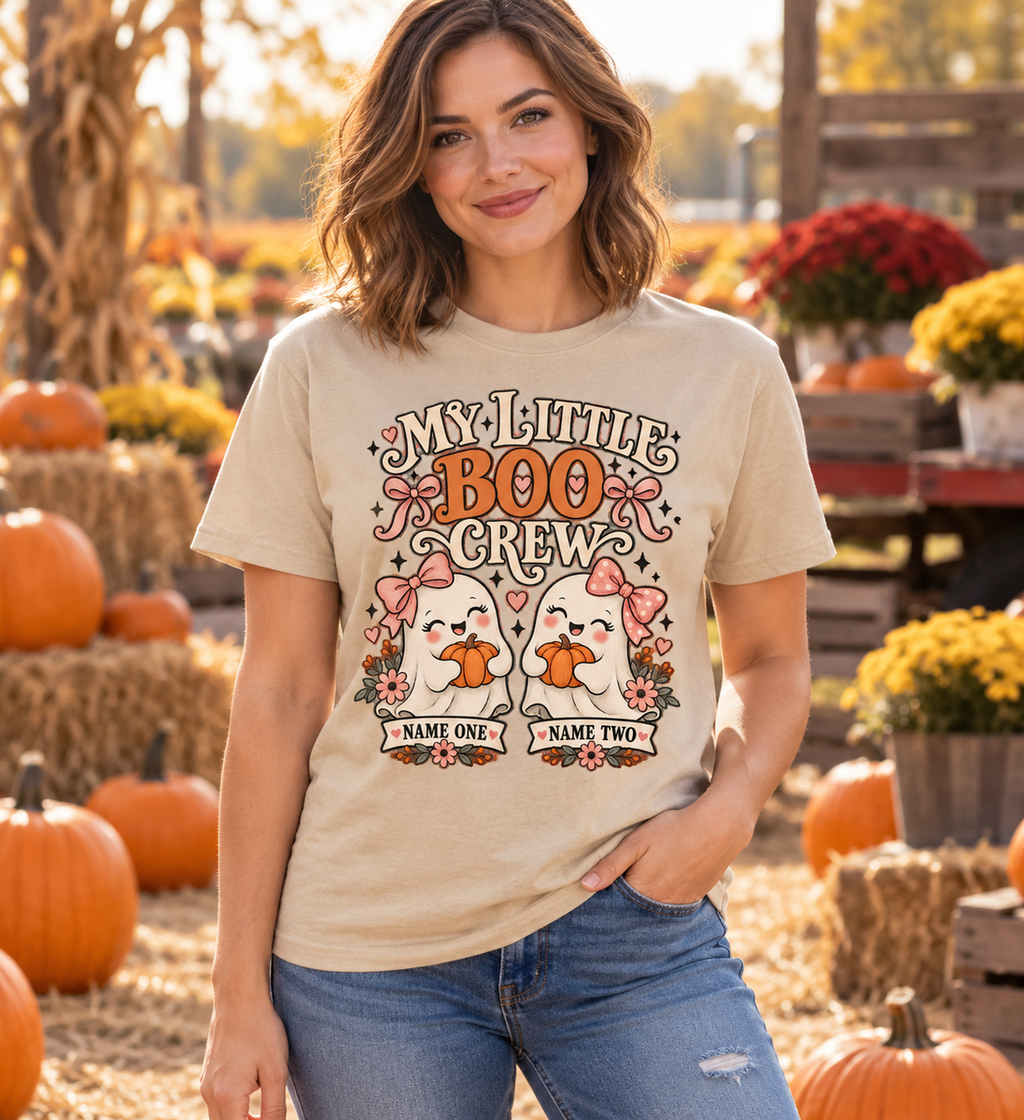 Illustrative lifestyle mockup: My Little Boo Crew personalized Halloween shirt with two name placeholders, Sand beige, worn by an adult woman.